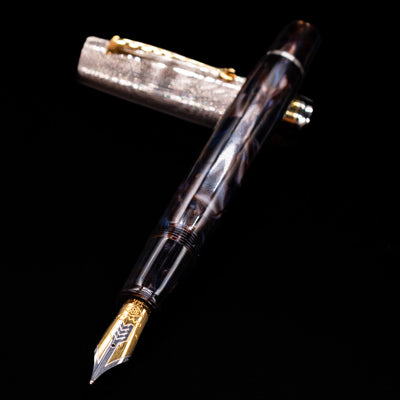 OMAS Bologna Fountain Pen - Galassia Argento laying across its own cap, crossed, with a focus on the nib.