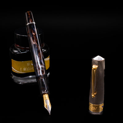 OMAS Bologna Fountain Pen - Galassia Argento leaning on an ink bottle uncapped showcasing the detailing on the nib.