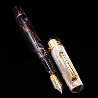 A full view of the OMAS Bologna Fountain Pen - Galassia Argento uncapped, with its cap laying next to the pen. 