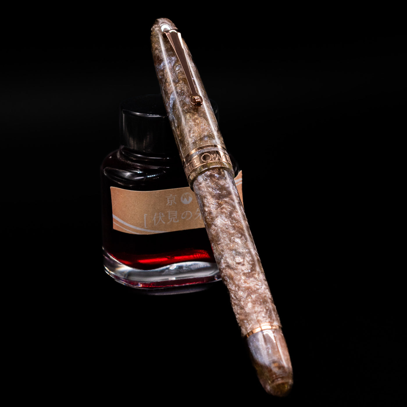 OMAS Ogiva Cocktail Series Fountain Pen - Espresso Martini capped, leaning against an ink bottle. 