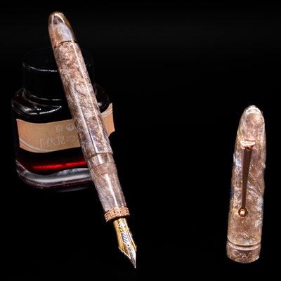 OMAS Ogiva Cocktail Series Fountain Pen - Espresso Martini leaning on an ink bottle uncapped showcasing the detailing on the nib.