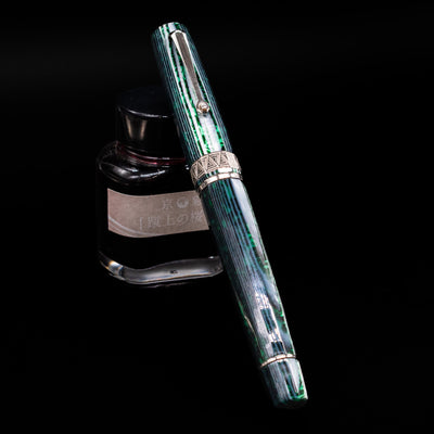 OMAS Paragon Fountain Pen - Arco Verde capped, leaning against an ink bottle.