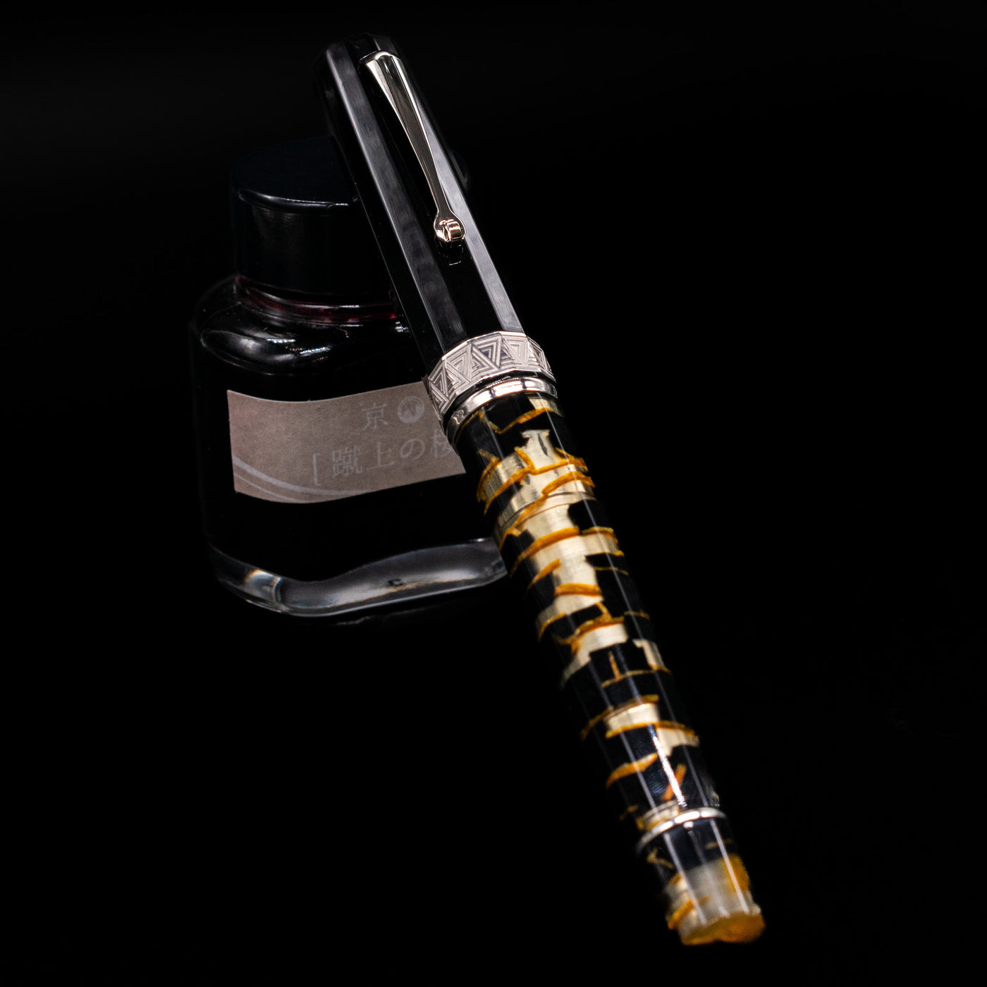 OMAS Paragon Fountain Pen - Black Lucen capped, leaning against an ink bottle. 