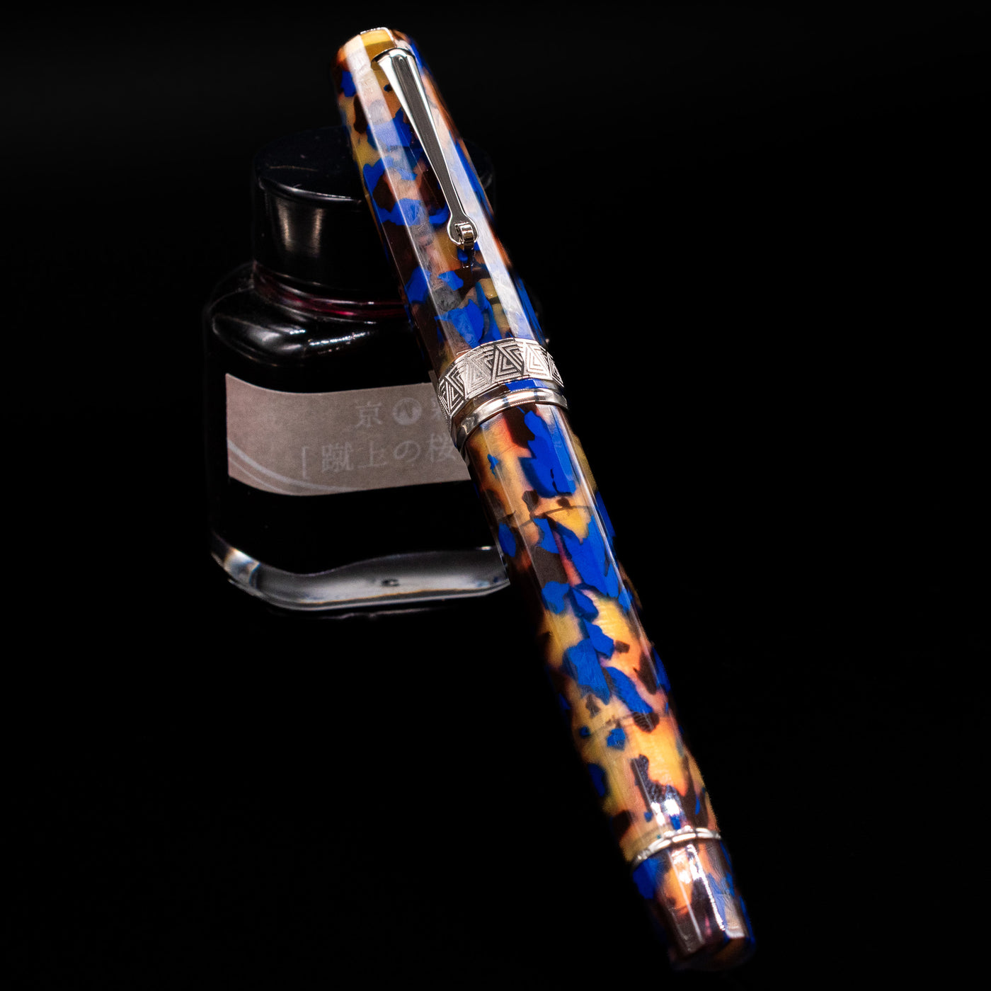 OMAS Paragon Fountain Pen - Blue Lucen capped, leaning against an ink bottle. 