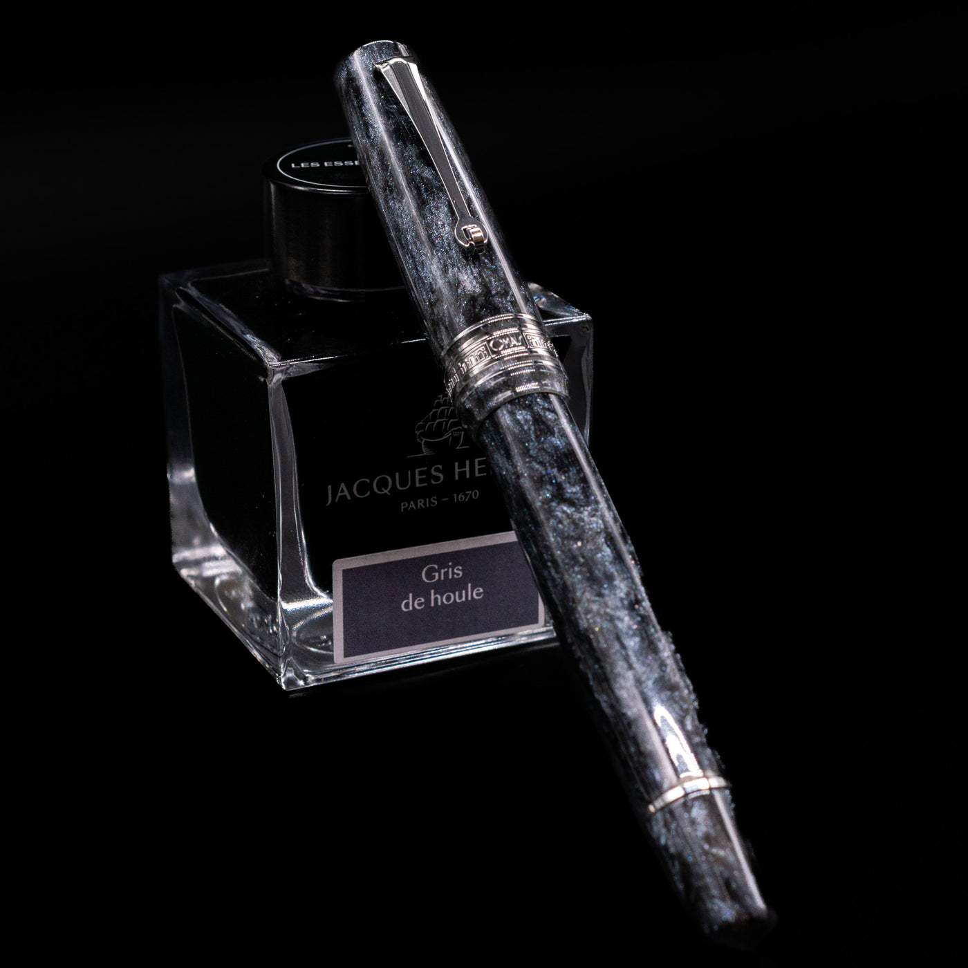 Omas Bologna Fountain Pen - Bright Grey capped, leaning against an ink bottle. 