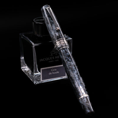 Omas Bologna Fountain Pen - Bright Grey capped, leaning against an ink bottle. 