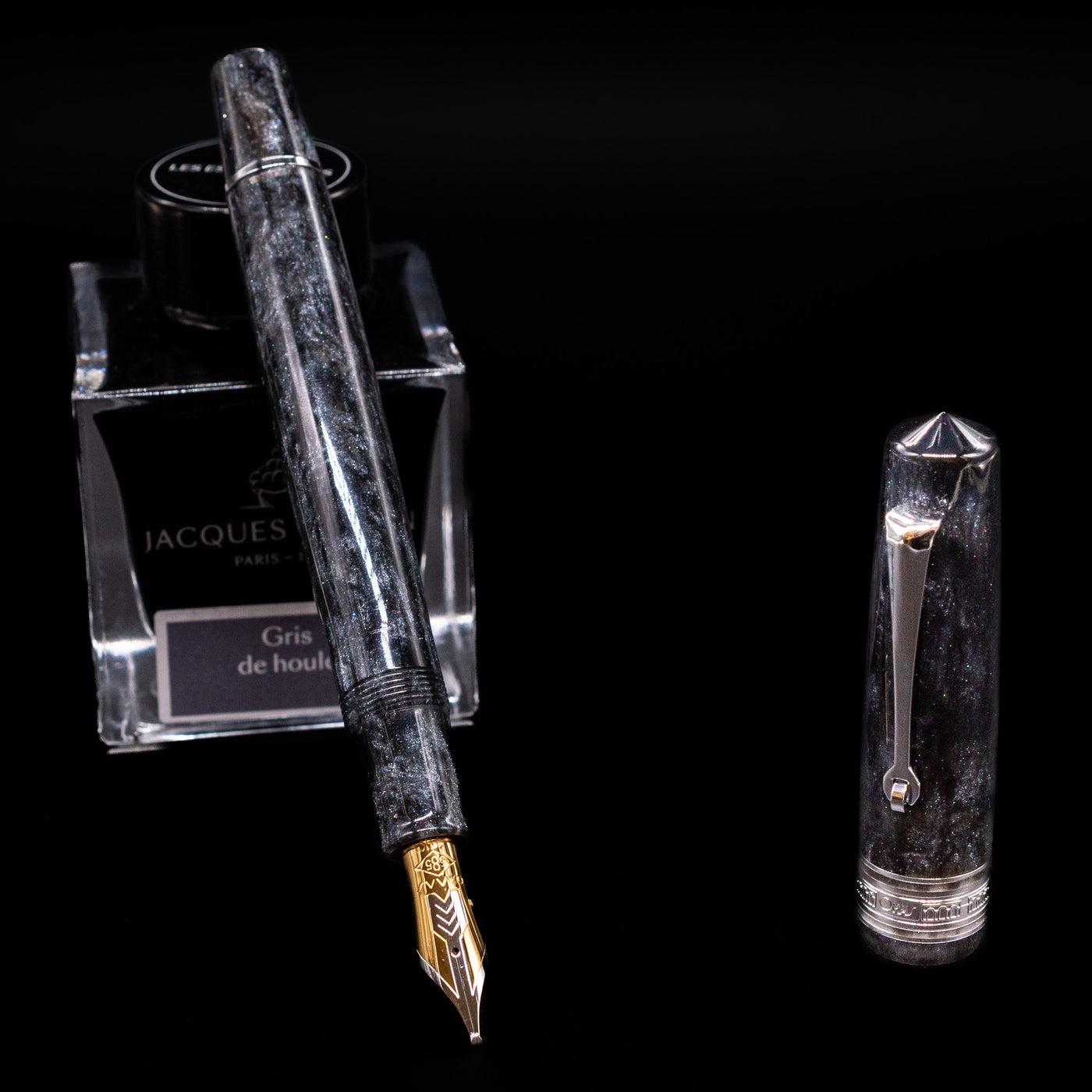 Omas Bologna Fountain Pen - Bright Grey leaning on an ink bottle uncapped showcasing the detailing on the nib.