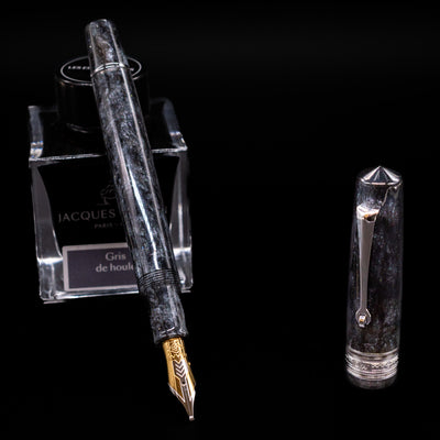 Omas Bologna Fountain Pen - Bright Grey leaning on an ink bottle uncapped showcasing the detailing on the nib.