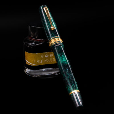 Omas Bologna Fountain Pen - Elegant Emerald capped, leaning against an ink bottle. 