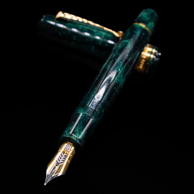 Omas Bologna Fountain Pen - Elegant Emerald laying across its own cap, crossed, with a focus on the nib.