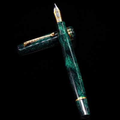 Omas Bologna Fountain Pen - Elegant Emerald laying on top of its cap in a crossed position showing full view of the entire uncapped pen.