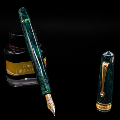 Omas Bologna Fountain Pen - Elegant Emerald leaning on an ink bottle uncapped showcasing the detailing on the nib.