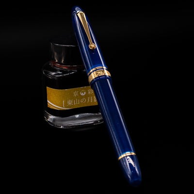 Omas Ogiva Fountain Pen - Blue Gold capped, leaning against an ink bottle. 