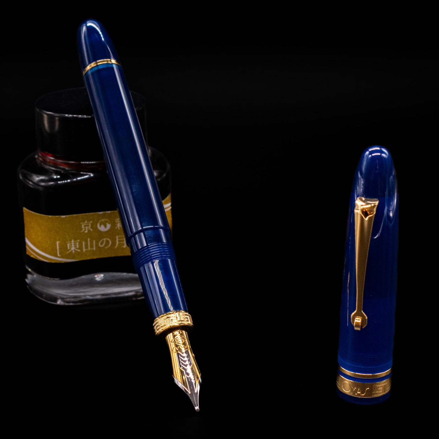 Omas Ogiva Fountain Pen - Blue Gold leaning on an ink bottle uncapped showcasing the detailing on the nib.