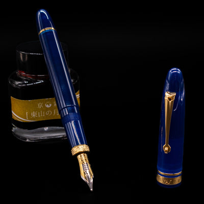 Omas Ogiva Fountain Pen - Blue Gold leaning on an ink bottle uncapped showcasing the detailing on the nib.