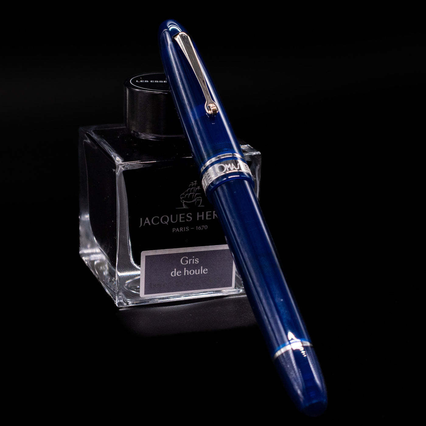 Omas Ogiva Fountain Pen - Blue Silver capped, leaning against an ink bottle. 
