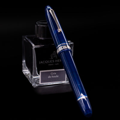 Omas Ogiva Fountain Pen - Blue Silver capped, leaning against an ink bottle. 