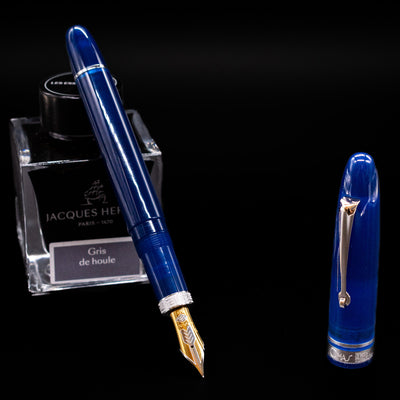 Omas Ogiva Fountain Pen - Blue Silver leaning on an ink bottle uncapped showcasing the detailing on the nib.