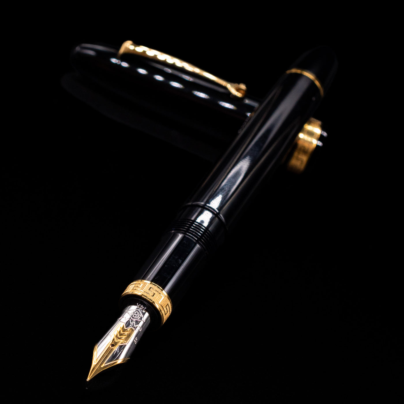 Omas Ogiva Fountain Pen - Nera Gold laying across its own cap, crossed, with a focus on the nib.