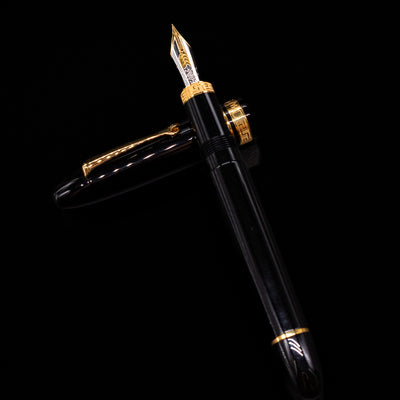Omas Ogiva Fountain Pen - Nera Gold laying on top of its cap in a crossed position showing full view of the entire uncapped pen.