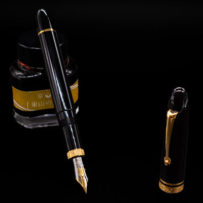 Omas Ogiva Fountain Pen - Nera Gold leaning on an ink bottle uncapped showcasing the detailing on the nib.