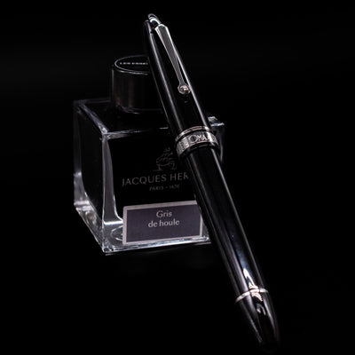 Omas Ogiva Fountain Pen - Nera Silver capped, leaning against an ink bottle. 