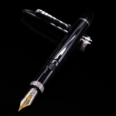 Omas Ogiva Fountain Pen - Nera Silver laying across its own cap, crossed, with a focus on the nib.