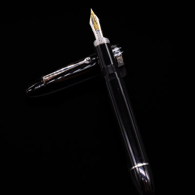 Omas Ogiva Fountain Pen - Nera Silver laying on top of its cap in a crossed position showing full view of the entire uncapped pen.