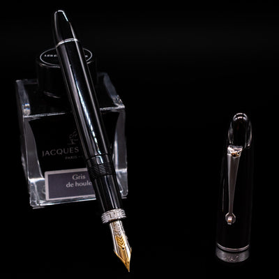 Omas Ogiva Fountain Pen - Nera Silver leaning on an ink bottle uncapped showcasing the detailing on the nib.