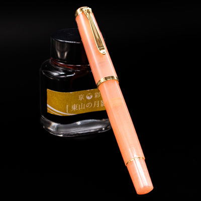 Pelikan Classic M200 Fountain Pen - Apricot Achat capped, leaning against an ink bottle. 