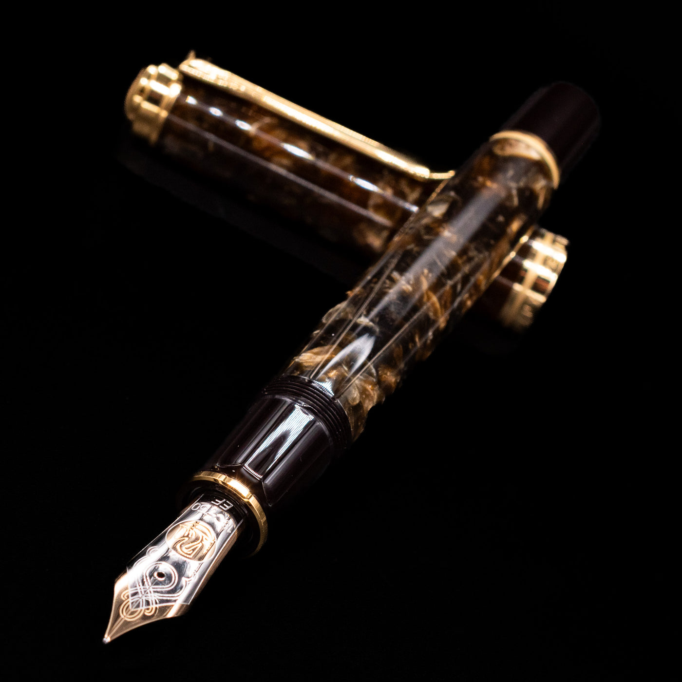 Pelikan Souverän M1000 Renaissance Brown fountain pen and cap crossed, with focus on the engraved 18k gold nib and the swirling marbled brown finish of the barrel.