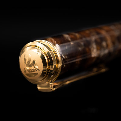 Close-up of the cap top on the Pelikan Souverän M1000 Renaissance Brown fountain pen, featuring the Pelikan logo medallion set into the glossy black resin finial with gold-plated trim.