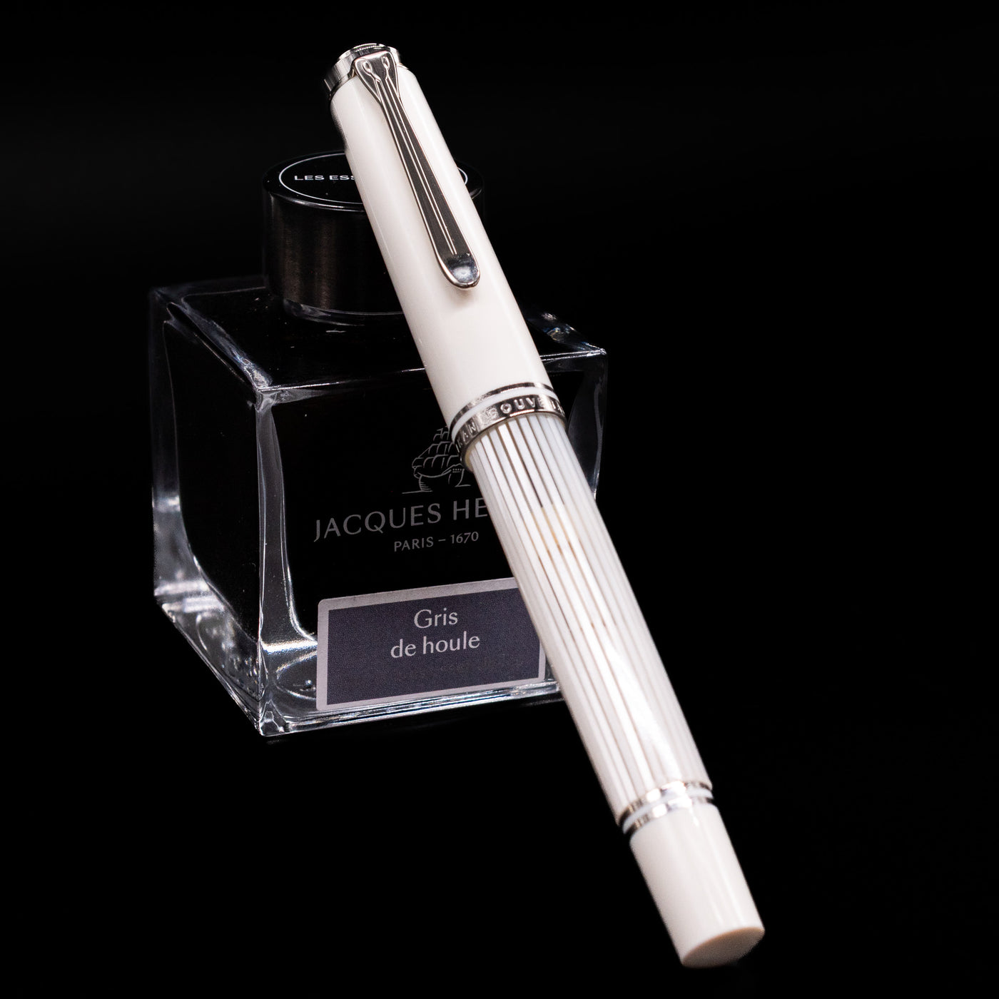 Pelikan Souverän M605 White Transparent fountain pen shown capped, resting at an angle against an ink bottle. The glossy white resin body features translucent barrel stripes with elegant palladium-plated trim.