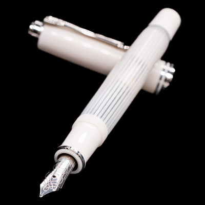 Pelikan Souverän M605 White Transparent fountain pen and cap crossed, with focus on the engraved rhodium-plated nib and the shimmering striped translucent barrel.