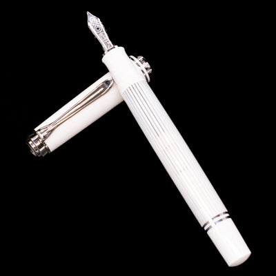 Pelikan Souverän M605 White Transparent fountain pen and cap arranged in a crossed position, highlighting the striped translucent barrel and contrasting polished white resin sections.