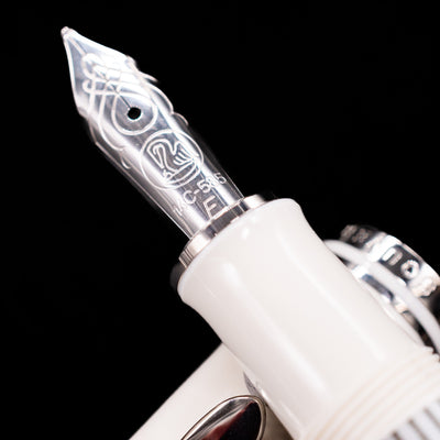 Close-up shot of the rhodium-plated 14k gold nib on the Pelikan Souverän M605 White Transparent fountain pen, showing detailed engravings and fine craftsmanship.