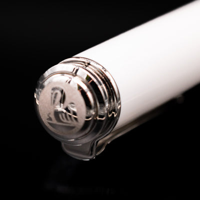 Close-up of the cap top on the Pelikan Souverän M605 White Transparent fountain pen, featuring the Pelikan logo medallion set into the glossy white resin finial with polished palladium trim.