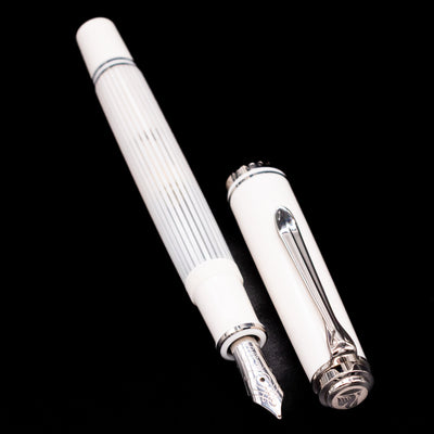 Pelikan Souverän M605 White Transparent fountain pen displayed uncapped, showcasing the white resin cap, translucent striped barrel, and rhodium-plated gold nib.