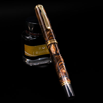 Pelikan Souveran M800 Fountain Pen - Grand Place capped, leaning against an ink bottle. 