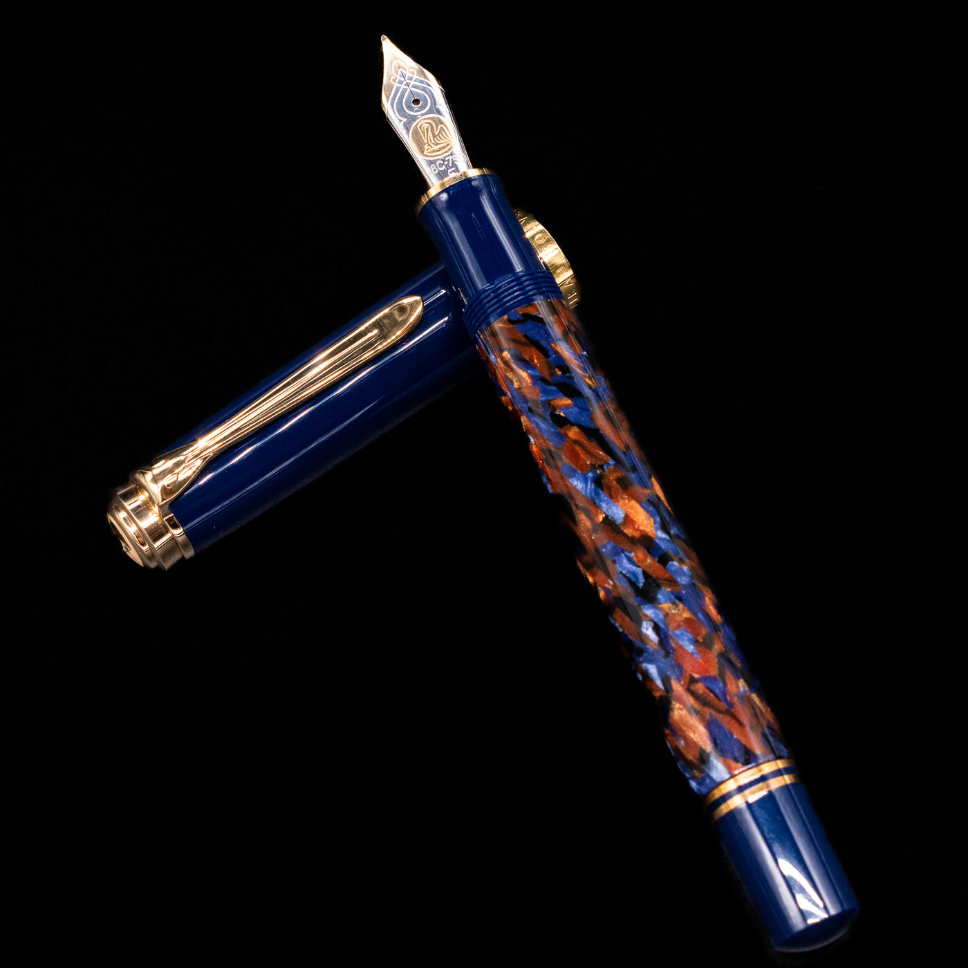 Preowned Pelikan Souverän M800 Stone Garden fountain pen and cap arranged in a crossed position, highlighting the marbled blue resin barrel, blue cap, and gold-plated clip and bands.