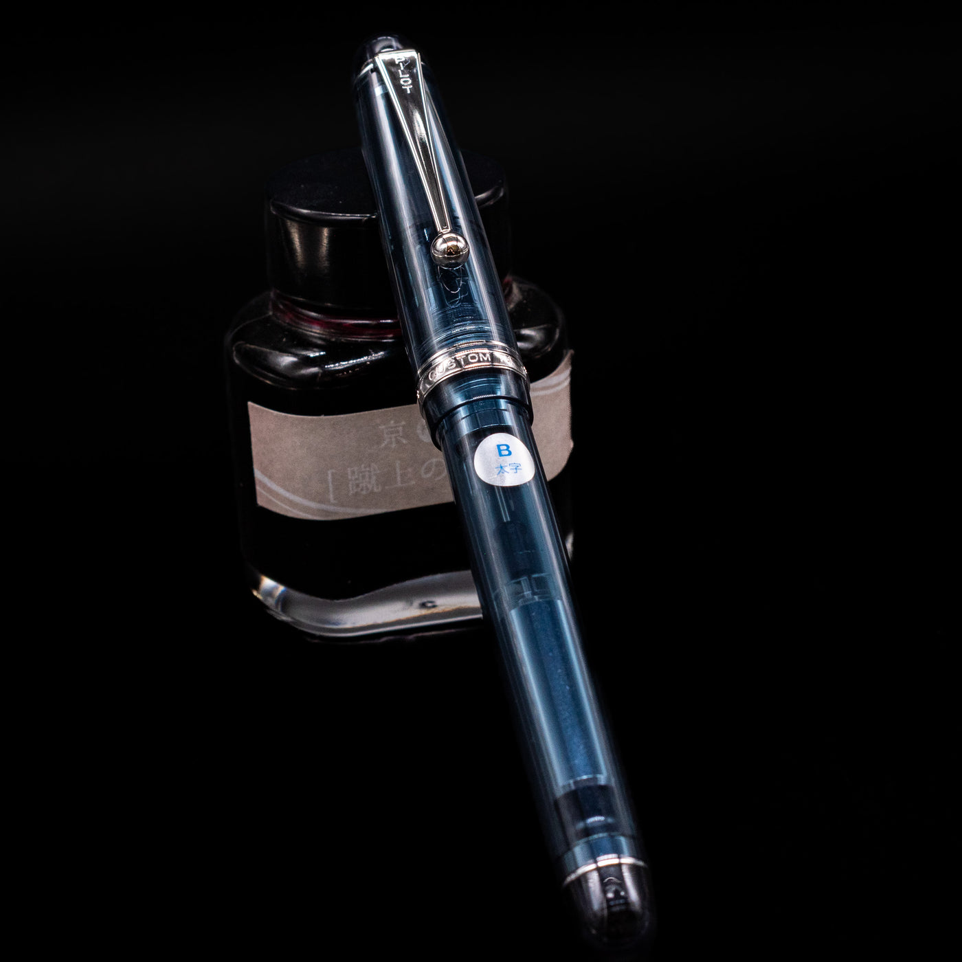 Pilot Custom 74 Fountain Pen - Blue Stone capped, leaning against an ink bottle. 