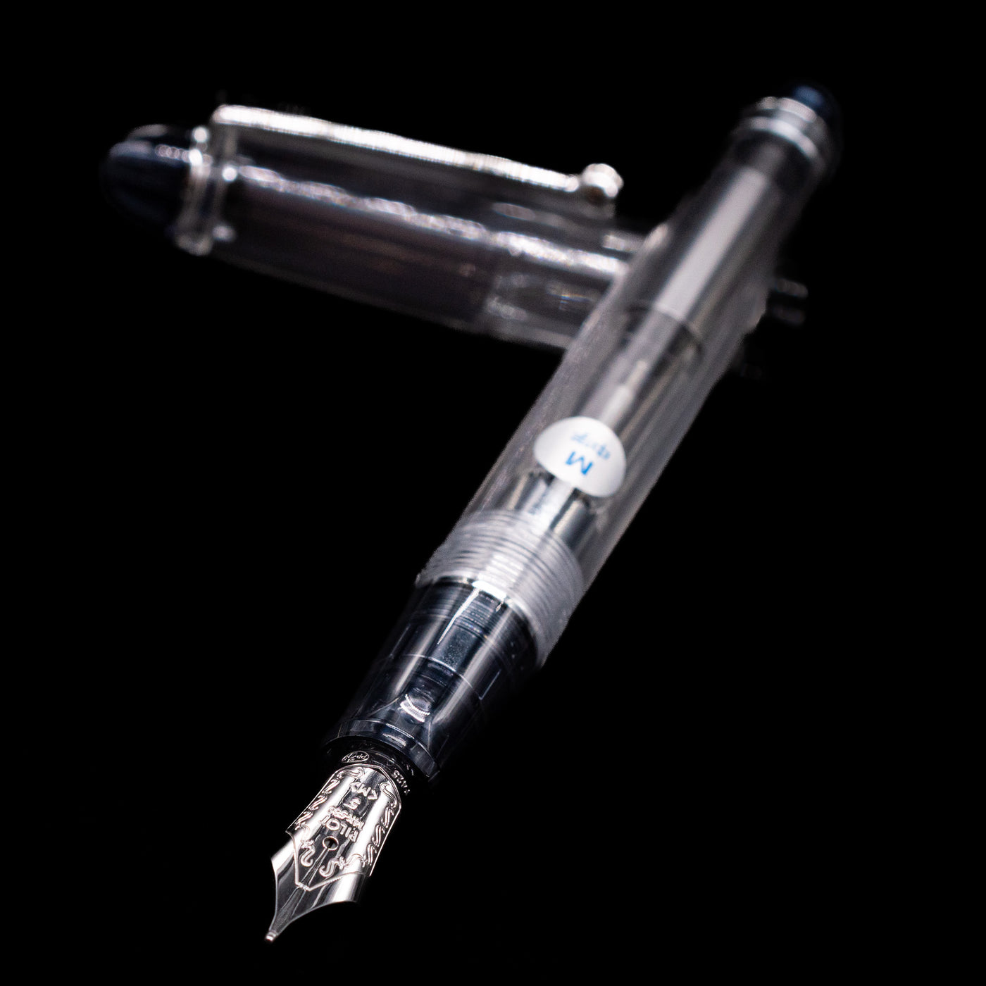 Pilot Custom 74 Fountain Pen - Clear laying across its own cap, crossed, with a focus on the nib.