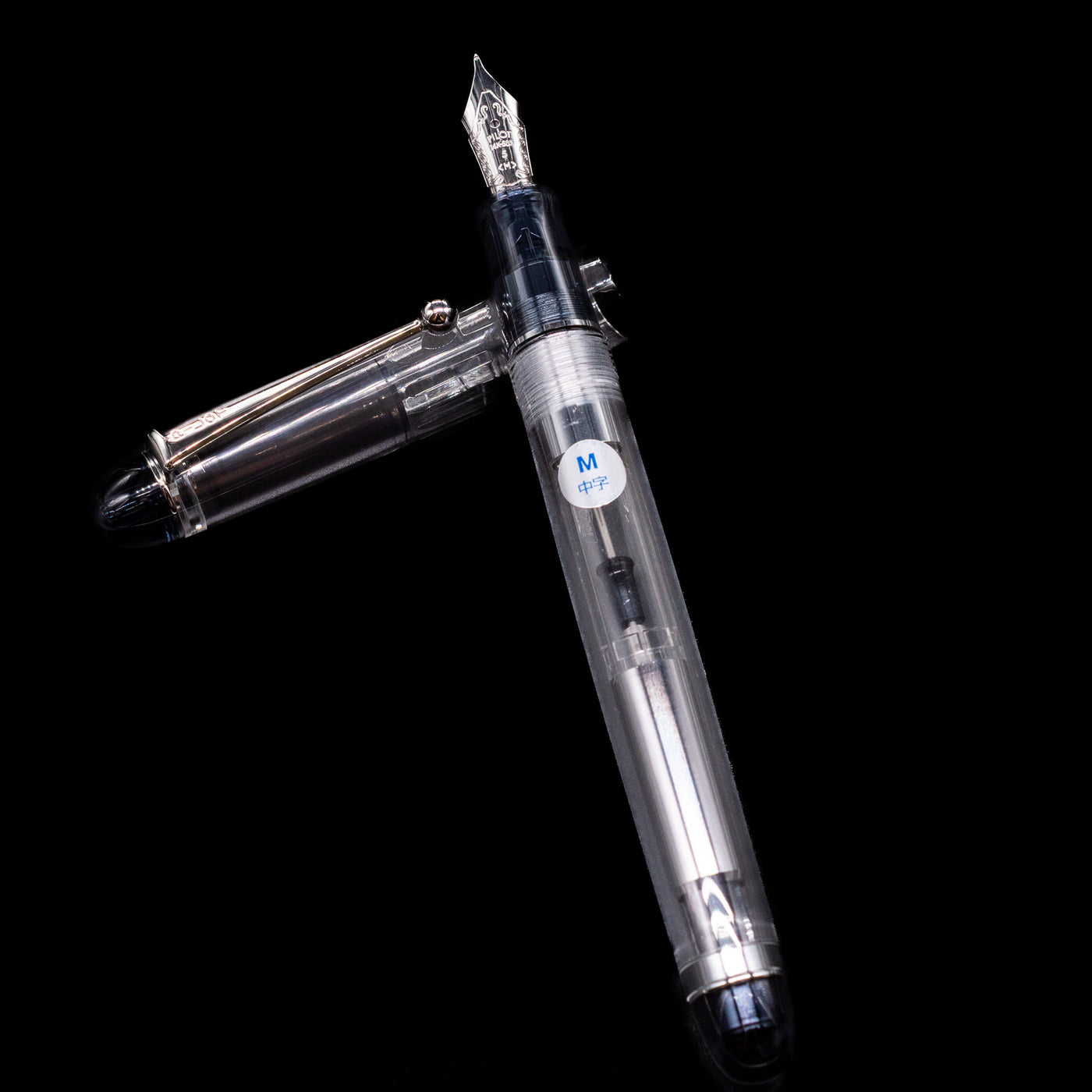 Pilot Custom 74 Fountain Pen - Clear  laying on top of its cap in a crossed position showing full view of the entire uncapped pen.