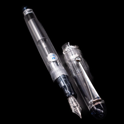 A full view of the Pilot Custom 74 Fountain Pen - Clear uncapped, with its cap laying next to the pen. 