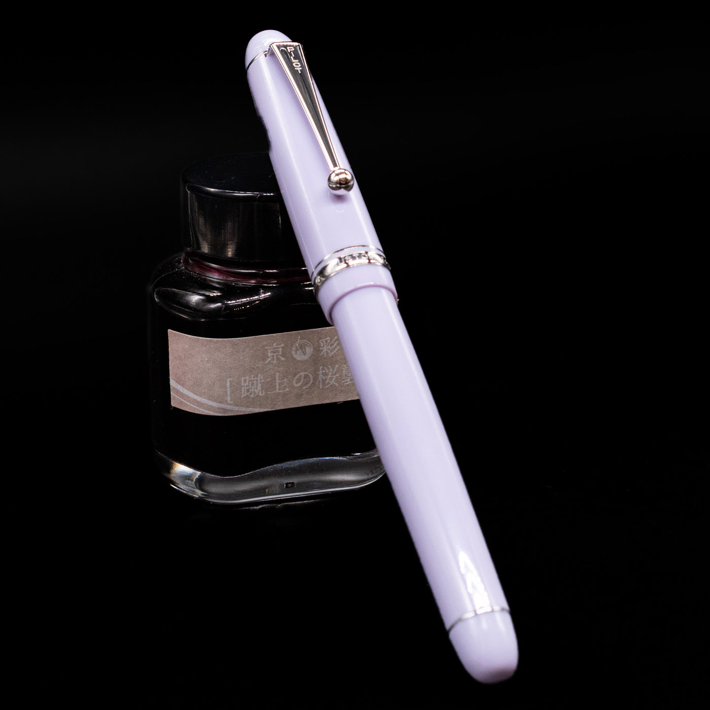 Pilot Custom 74 Fountain Pen - Lavender Fog capped, leaning against an ink bottle. 