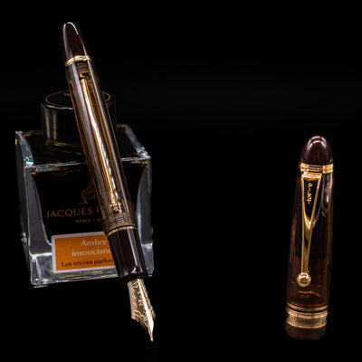 Pilot Custom 823 Amber Fountain Pen leaning on an ink bottle uncapped showcasing the detailing on the nib.