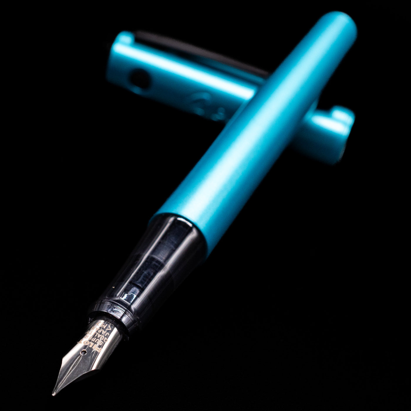 Pilot Explorer Turquoise Blue Metal Fountain Pen laying across its own cap, crossed, with a focus on the nib