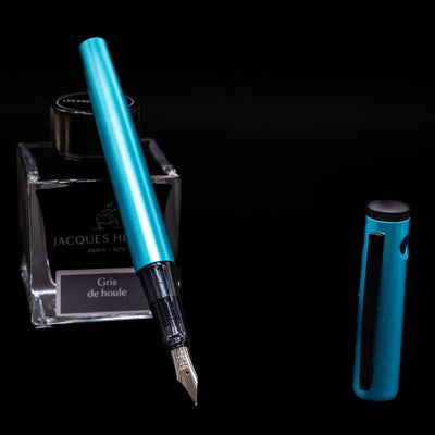 Pilot Explorer Turquoise Blue Metal Fountain Pen leaning on an ink bottle uncapped showcasing the detailing on the nib.