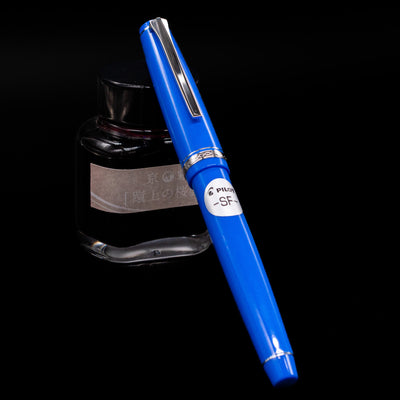 Pilot Falcon Fountain Pen - Blue capped, leaning against an ink bottle. 
