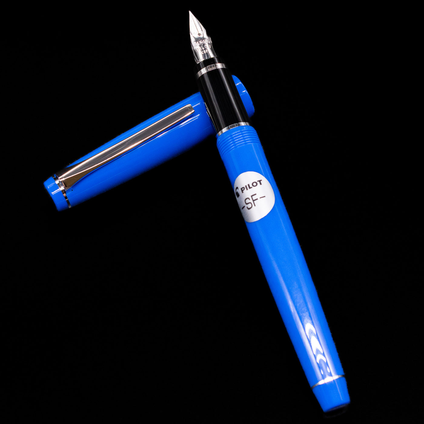 Pilot Falcon Fountain Pen - Blue laying on top of its cap in a crossed position showing full view of the entire uncapped pen.